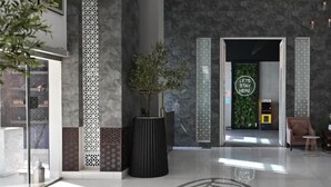 A modern lobby with a large potted plant, a reception desk, and a 'Let's Stay Here' sign. - Ayan Hotel (Riyadh)