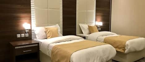 Habitación de hotel con dos camas, cabecero de madera, mesita de noche y alfombra estampada.