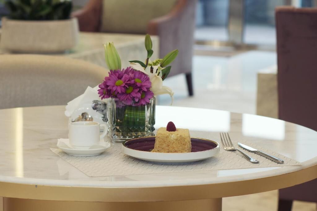 A round table with a white cup, a plate with a dessert, and a vase with flowers.