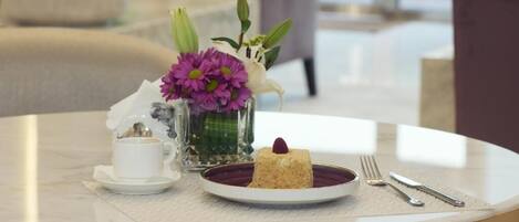 A round table with a white cup, a plate with a dessert, and a vase with flowers.