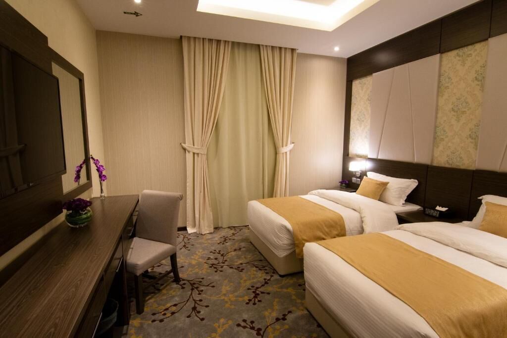 A hotel room with two beds, a desk, a chair, and a large mirror.