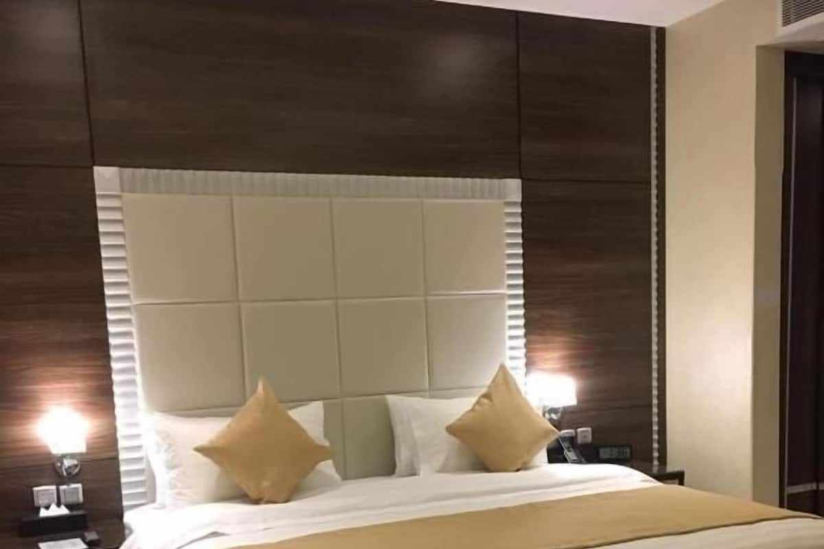 Quarto de hotel com uma cama grande, cabeceira, duas mesinhas de cabeceira e um tapete com padrão floral.