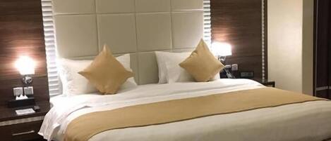 Une chambre d’hôtel avec un grand lit, une tête de lit, deux tables de chevet et une moquette à motifs floraux.