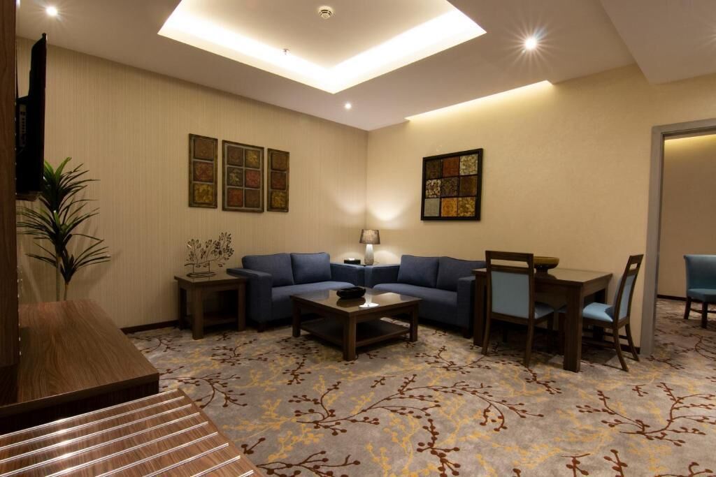 A hotel room with a living area featuring a sofa set, a coffee table, a TV, and a decorative plant.
