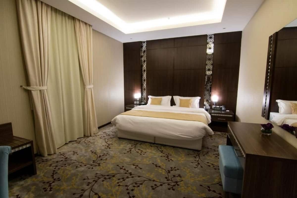 Quarto de hotel com cama grande, escrivaninha, cadeira e espelho.