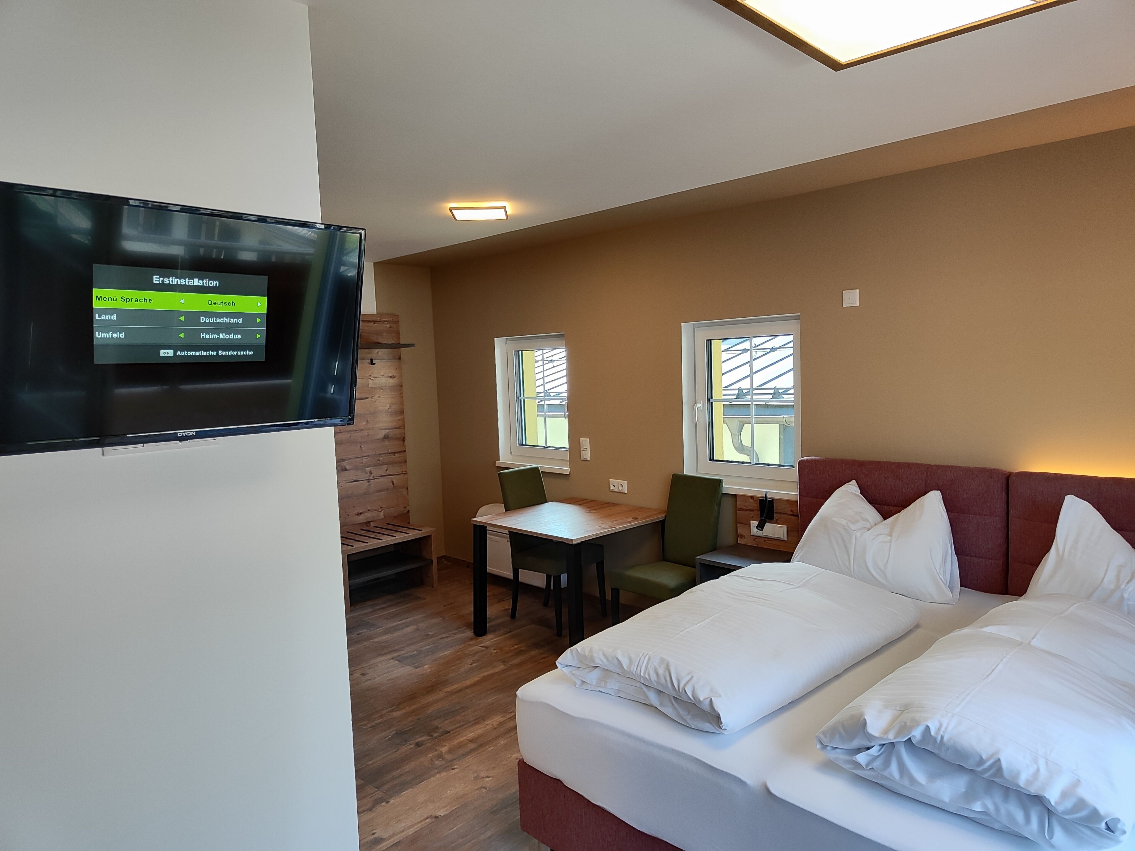 A hotel room with a bed, a desk, a chair, and a TV displaying a language selection menu.