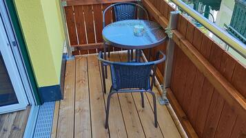 A wooden deck with a round table and two chairs, a metal railing, and a view of neighboring houses.