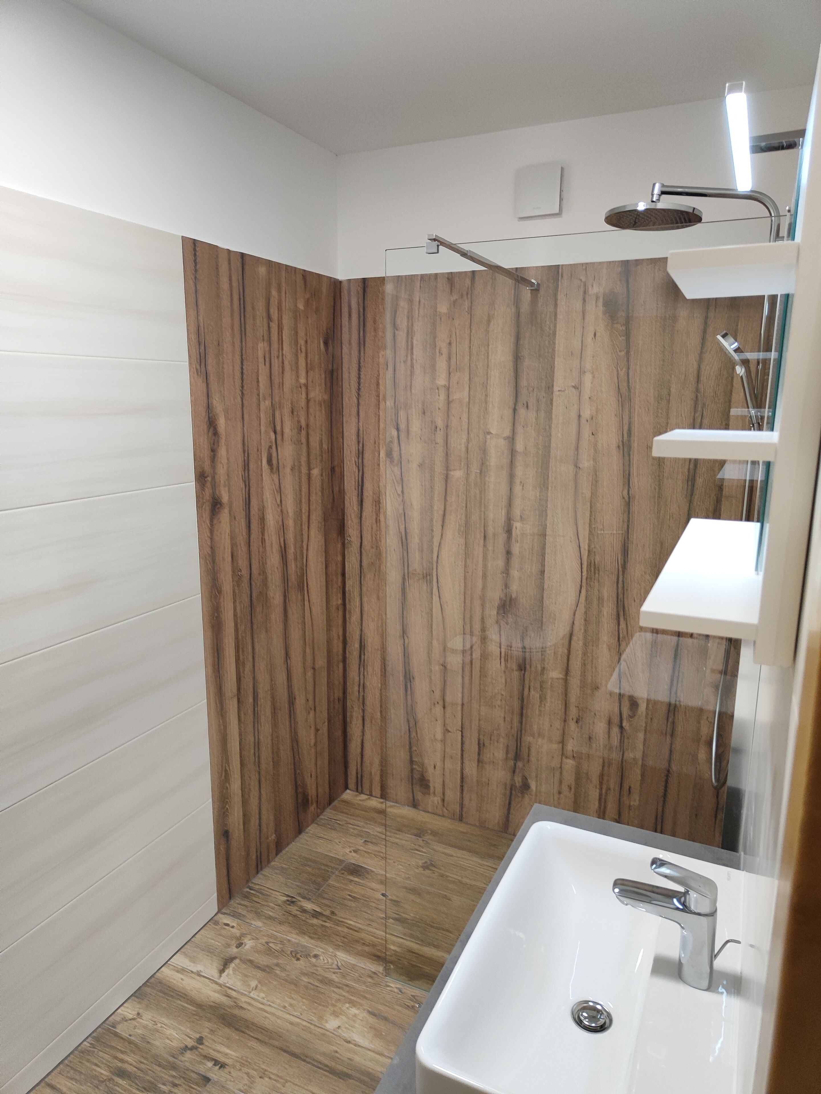 Une salle de bain moderne avec un mur d’accent en bois, un lavabo blanc et une cabine de douche en verre.