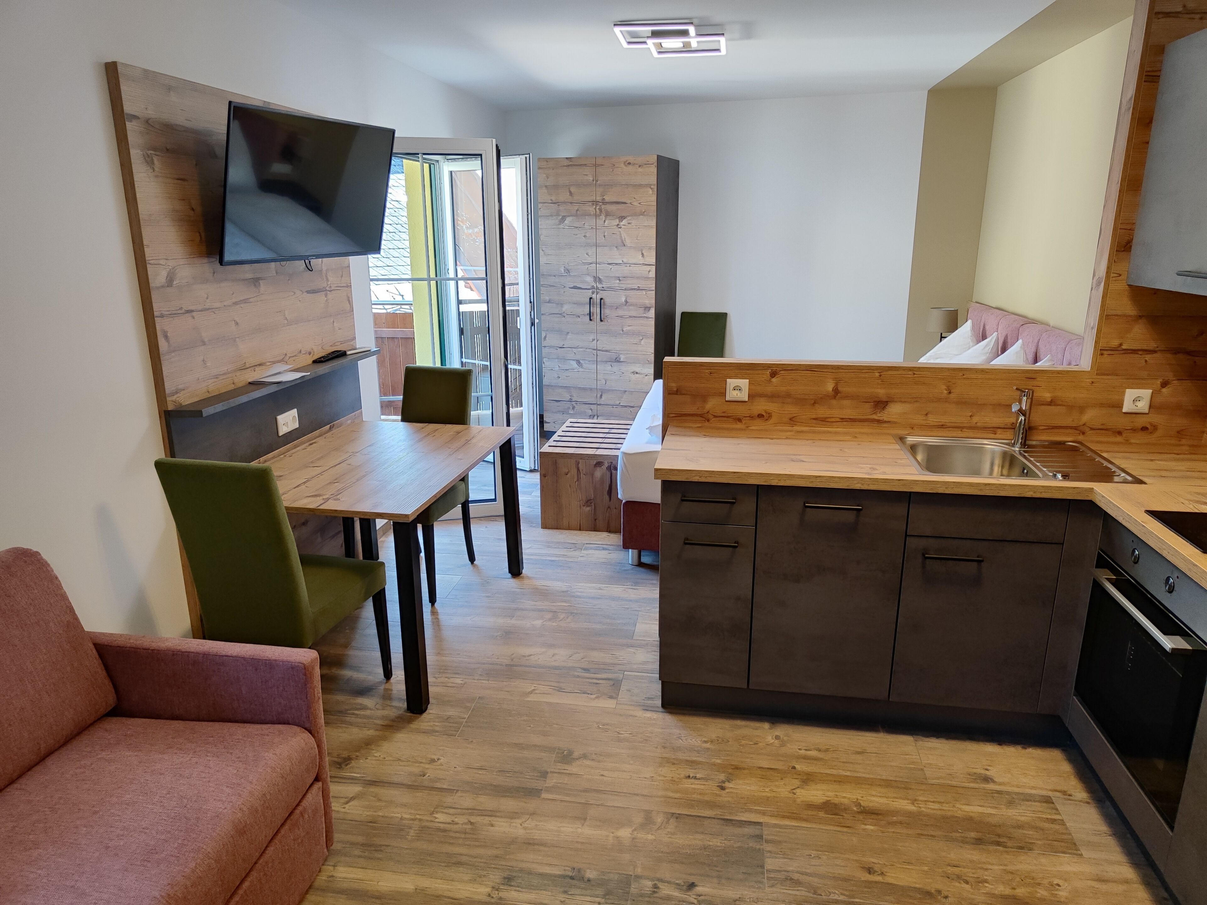 Una cocina moderna con armarios de madera, horno empotrado y zona de comedor con mesa y sillas.