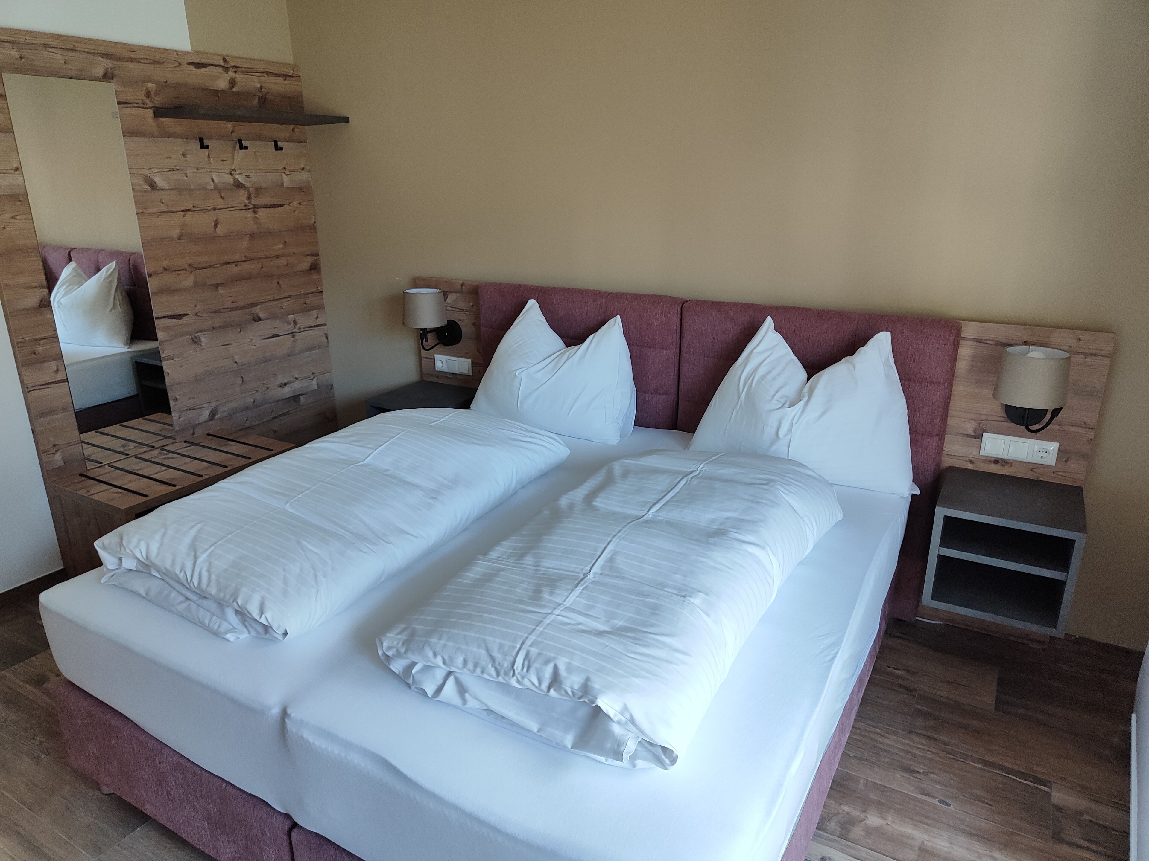Cama doble con ropa de cama blanca, dos mesitas de noche con lámparas, cabecera de madera y un espejo en la pared izquierda.