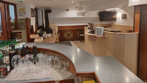 A bar area with a counter, glasses, and bottles. There is a television on the wall and a wooden staircase in the background. - Hotel Bad goisern (Bad Goisern)