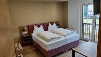 A double bed with white linens, a wooden nightstand, a bedside table, and a view of the outside through a sliding glass door.