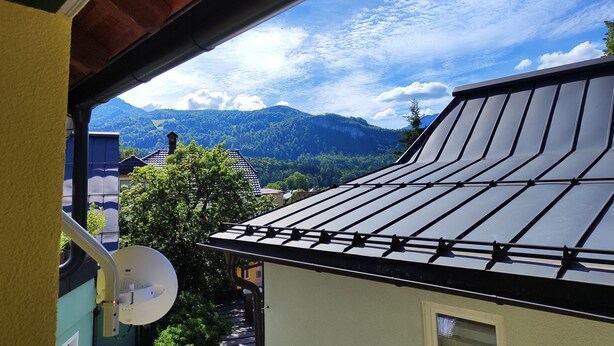 A view from a balcony with a mountain backdrop, a satellite dish, and a building with a sloped roof. - Hotel Bad goisern (Bad Goisern)