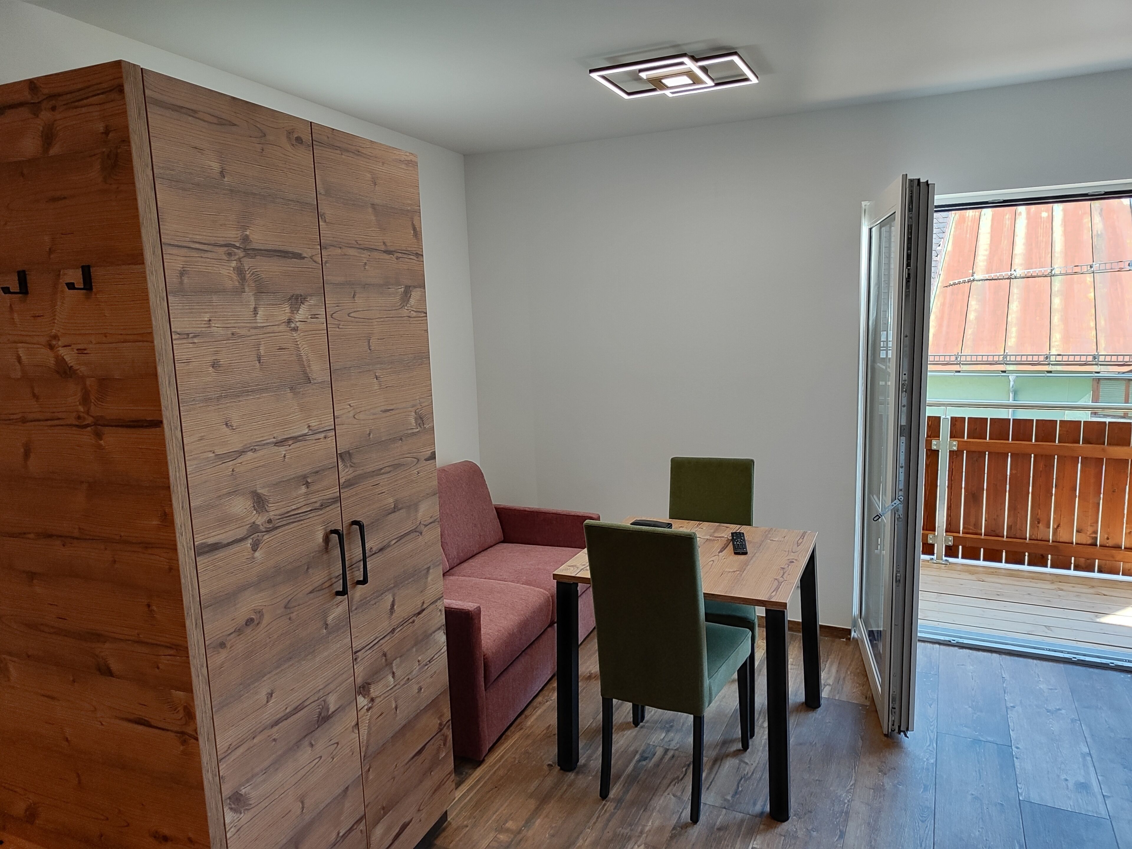 Una habitación con un armario de madera, una pequeña mesa con silla y una puerta de cristal corredera que da a un espacio al aire libre.