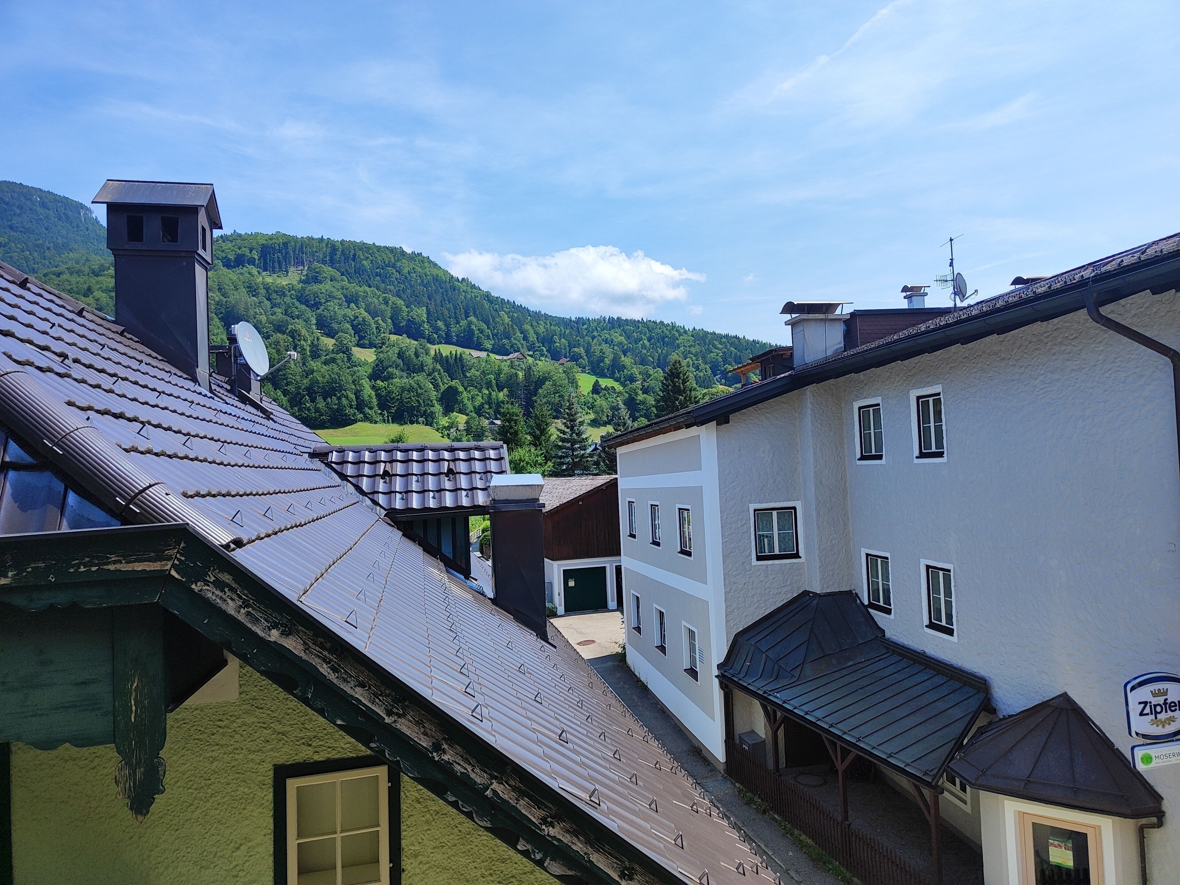 Ein traditionelles Gebäude mit einem geneigten Dach, einem kleinen turmartigen Aufbau und einem Schild, das auf ein lokales Geschäft hinweist.