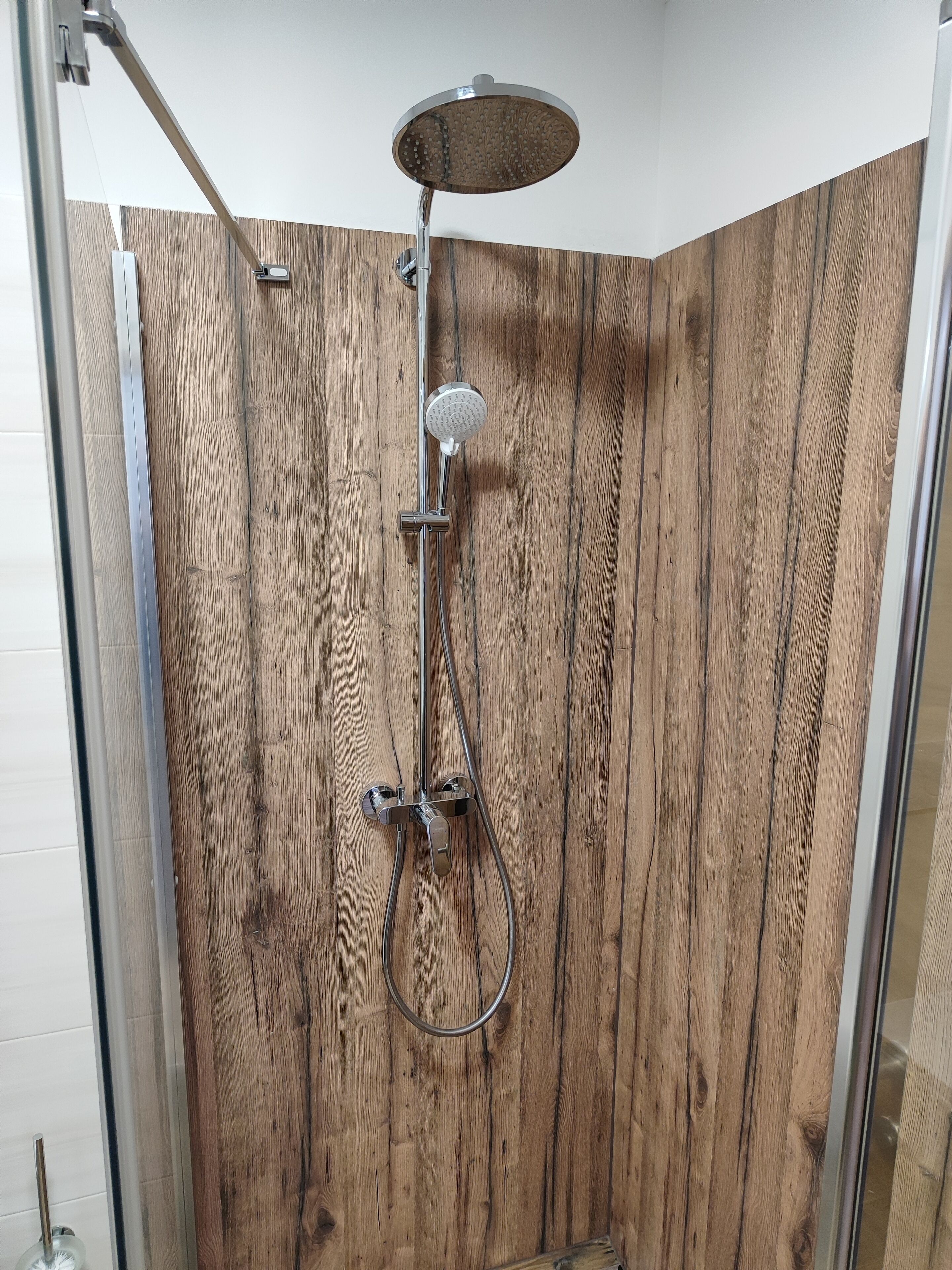 A shower with a wooden panel wall, a handheld showerhead, and a wall-mounted faucet.