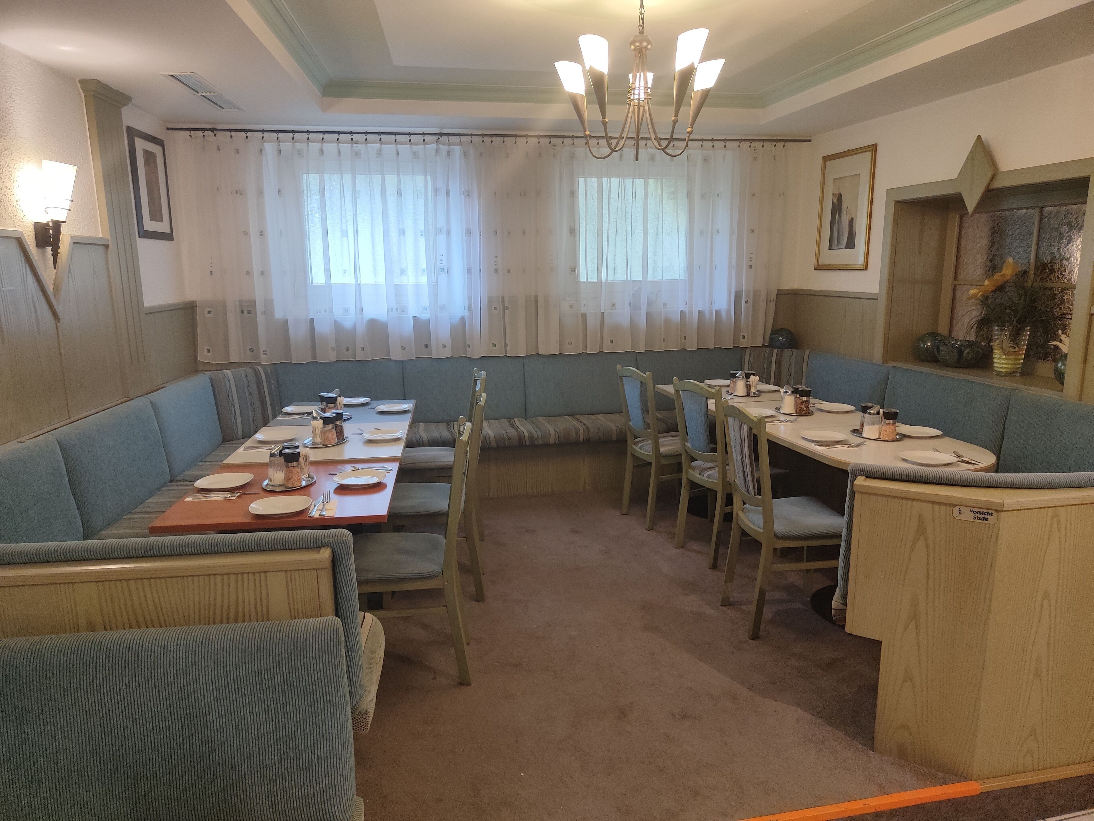 Uma área de refeições com uma mesa comprida posta para quatro pessoas, rodeada por assentos acolchoados azuis.