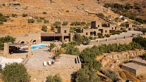 A hillside property with stone buildings, a swimming pool, and a paved area with lounge chairs. - Andros Serenity Retreat - Adults Only (Andros)