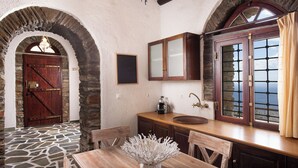 A rustic kitchen with stone walls, wooden cabinets, and a large window with curtains. - Andros Serenity Retreat - Adults Only (Andros)