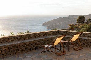 A stone wall with two wooden chairs facing a scenic view of the sea and a rocky landscape. - Andros Serenity Retreat - Adults Only (Andros)
