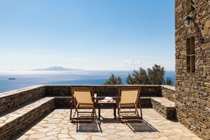 A stone patio with two wooden chairs and a table, overlooking a scenic view of the sea and a mountain. - Andros Serenity Retreat - Adults Only (Andros)