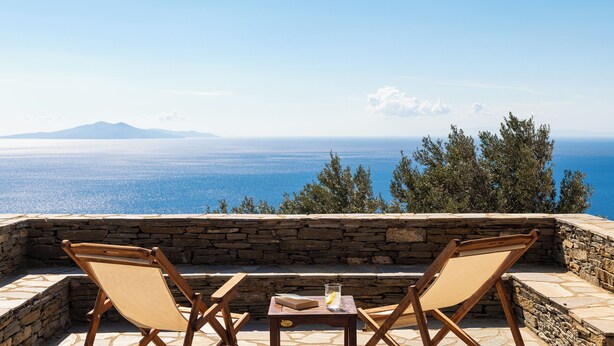 A stone wall with two wooden chairs facing a scenic view of the sea and a mountain. - Andros Serenity Retreat - Adults Only (Andros)