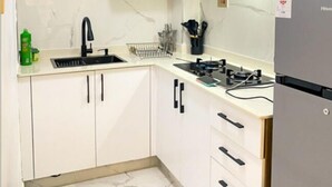 Une cuisine de taille réduite avec des meubles blancs, un évier en acier inoxydable et une cuisinière à gaz.