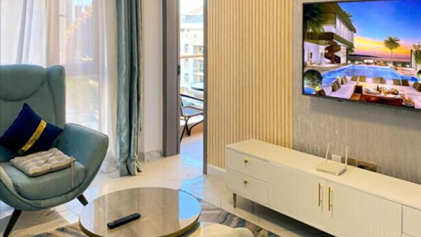 Une chambre d’hôtel moderne dotée d’une grande télévision, d’un fauteuil confortable, d’une table basse ronde et offrant une vue sur la ville par la fenêtre.