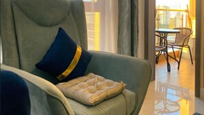 Un salon moderne avec un fauteuil gris, un coussin à motifs et une vue sur un balcon extérieur aménagé en espace repas.