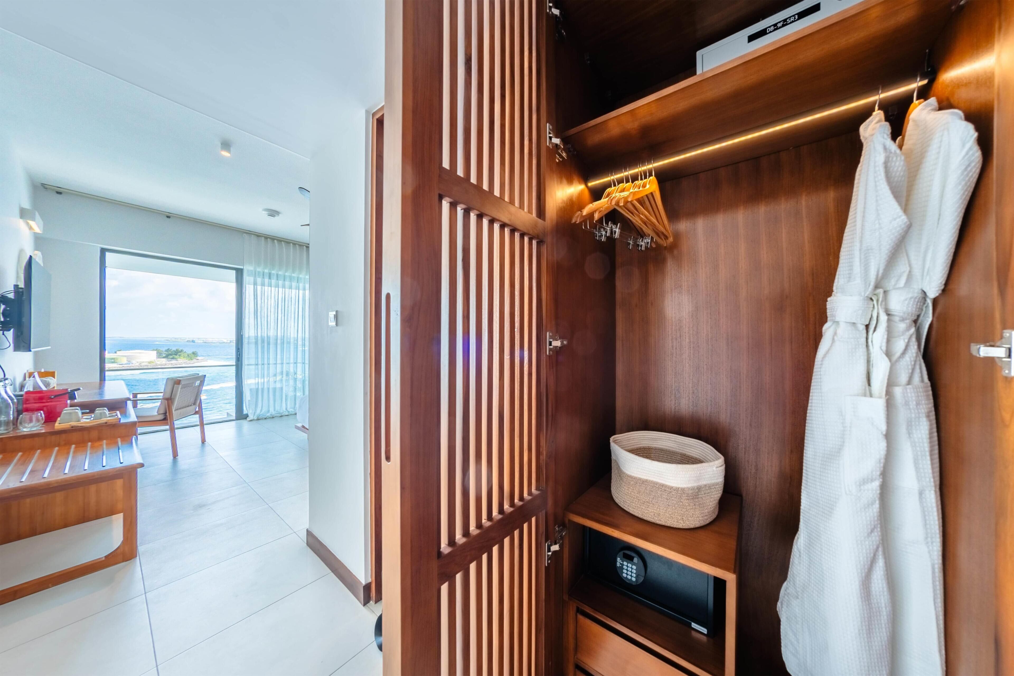 Habitación de hotel con armario de madera, zona de comedor con mesa y sillas, y vista al mar.
