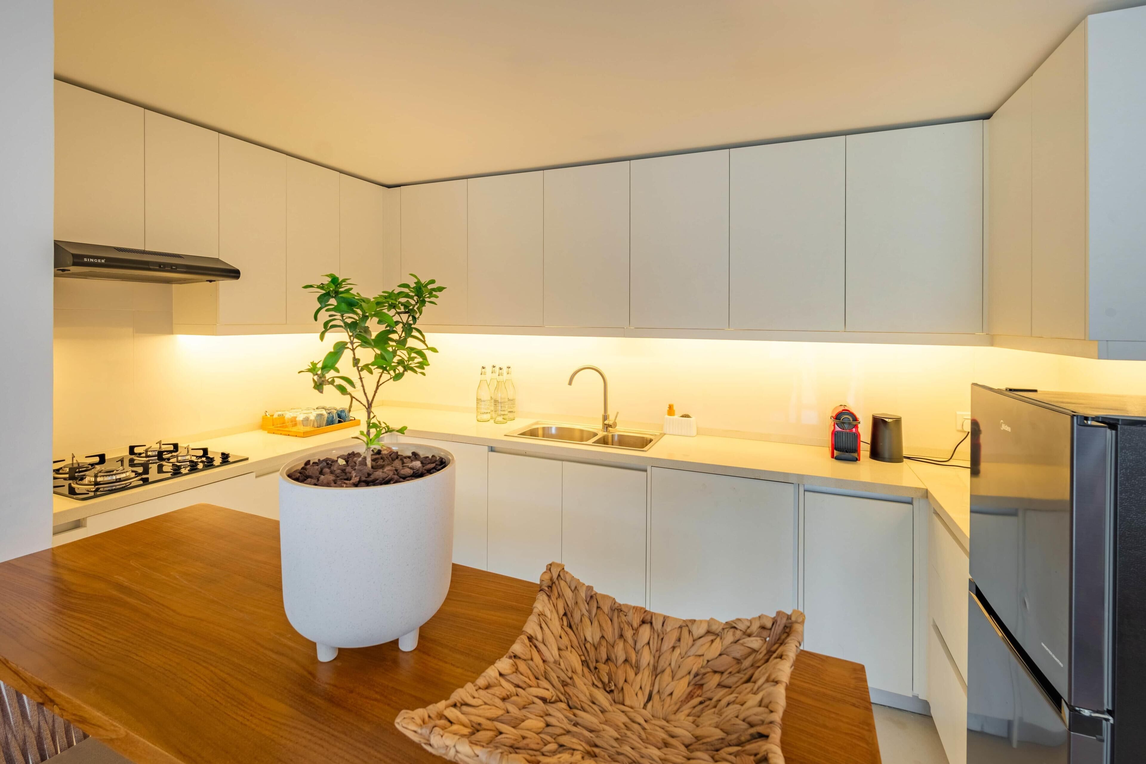A modern kitchen with white cabinets, a central island with a potted plant, a built-in stove, and a stainless steel refrigerator.