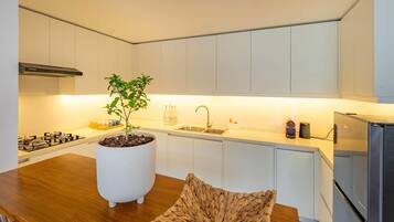 A modern kitchen with white cabinets, a central island with a potted plant, a built-in stove, and a stainless steel refrigerator.