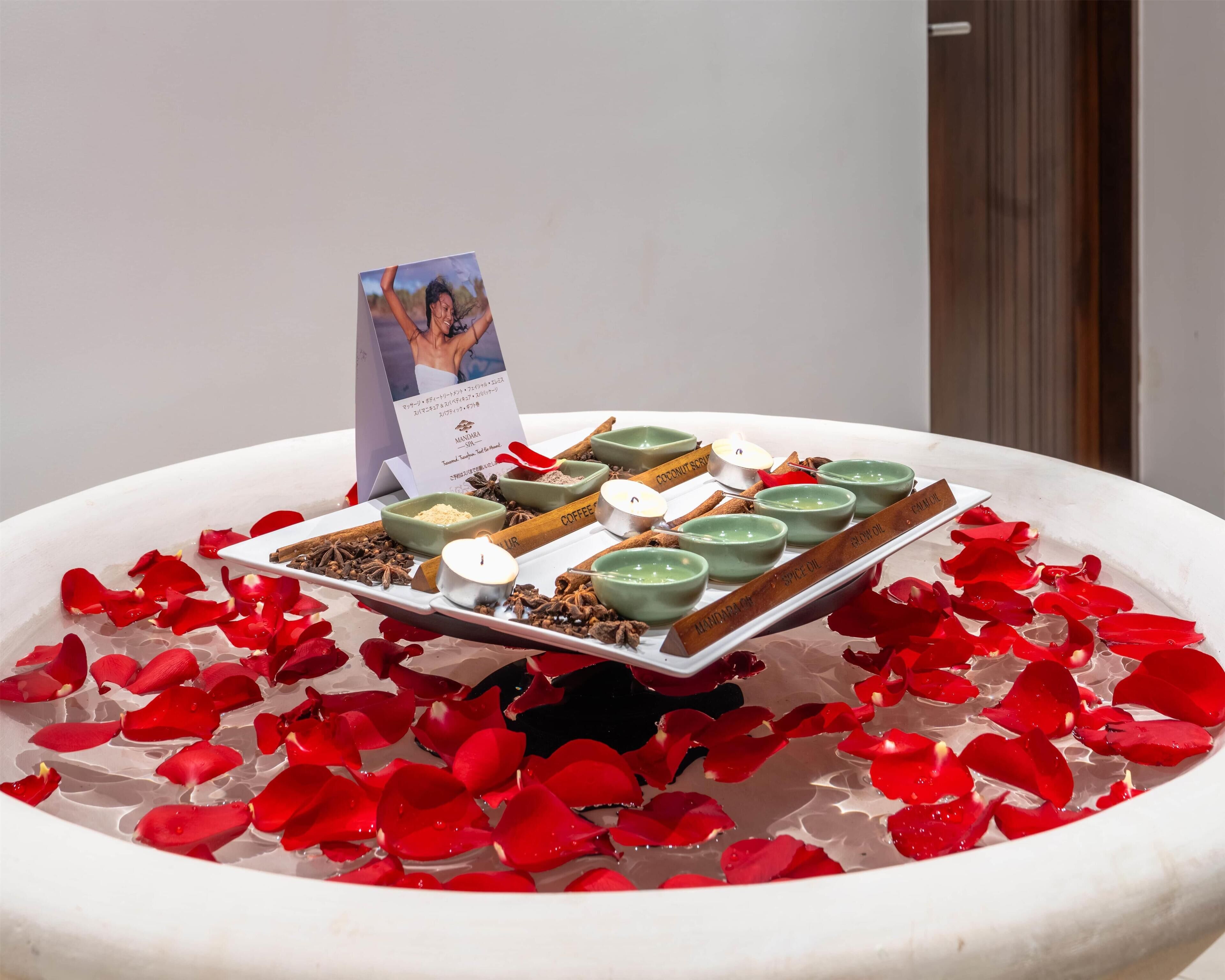 A display of scented oils with labels such as "Coconut Oil," "Coffee," and "Spice Oil" on a white tray surrounded by rose petals.
