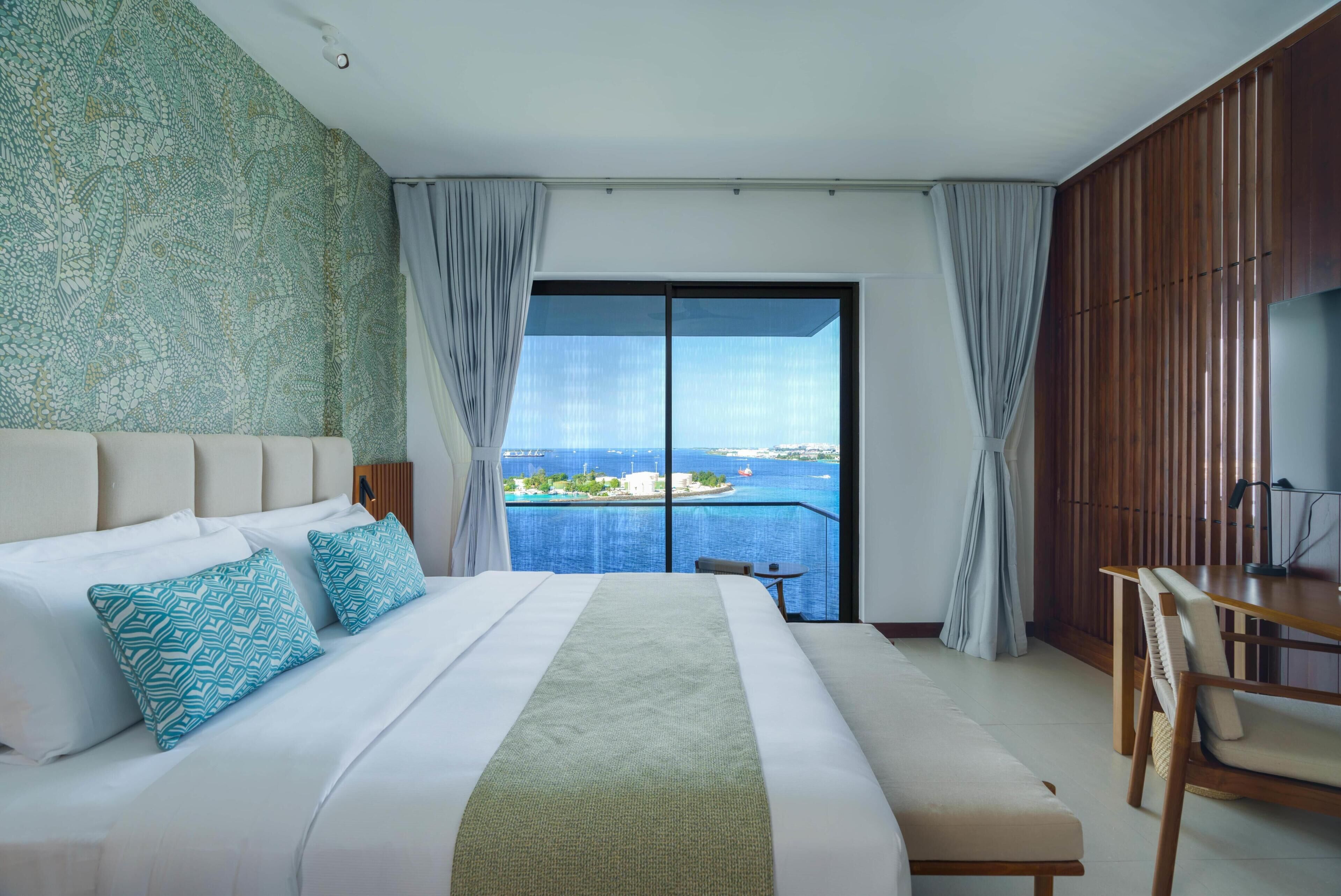 Habitación de hotel con una cama grande, un escritorio y vista al mar.