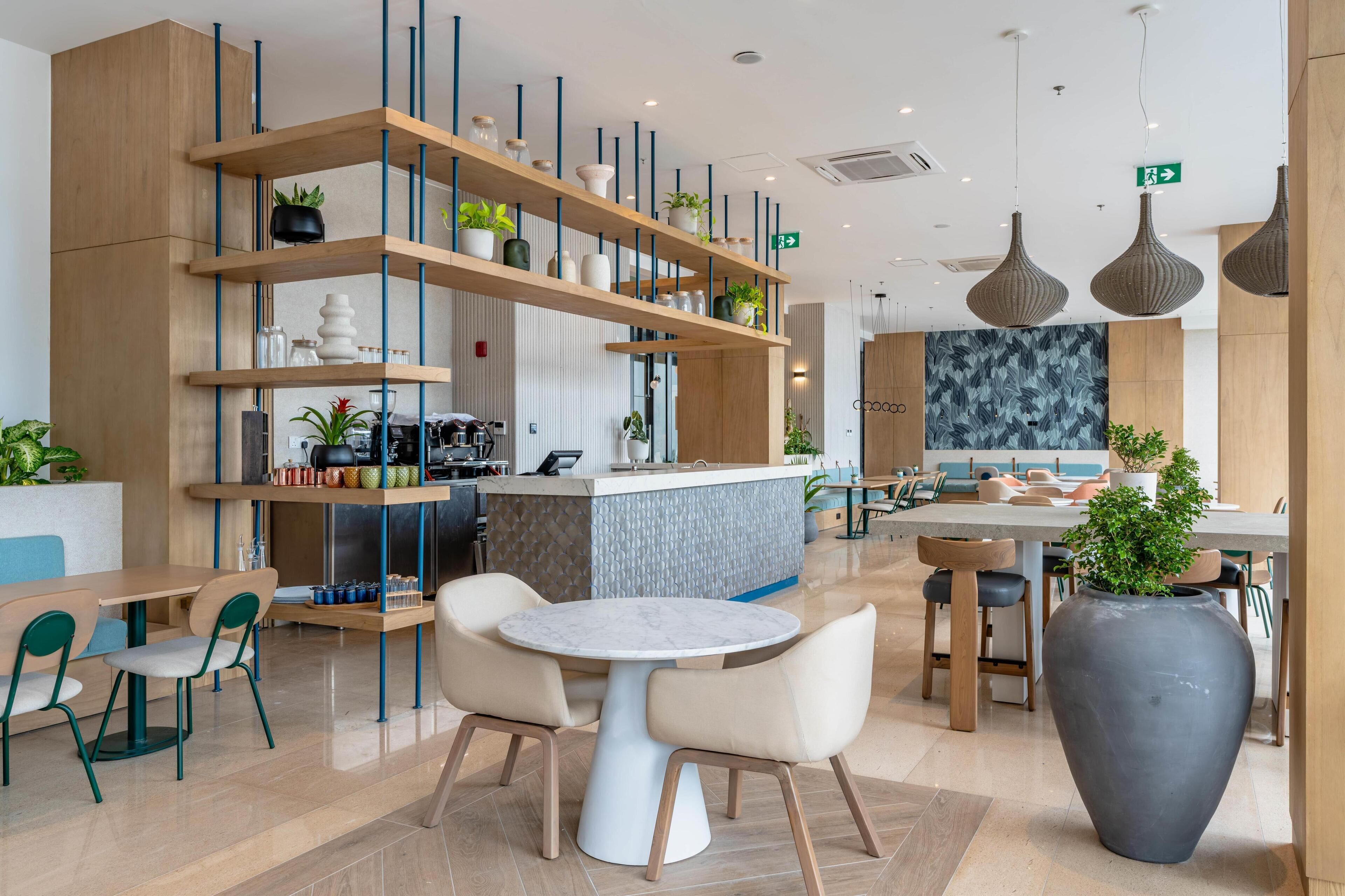 A modern cafe with a central round table, bar area, and seating with plants.