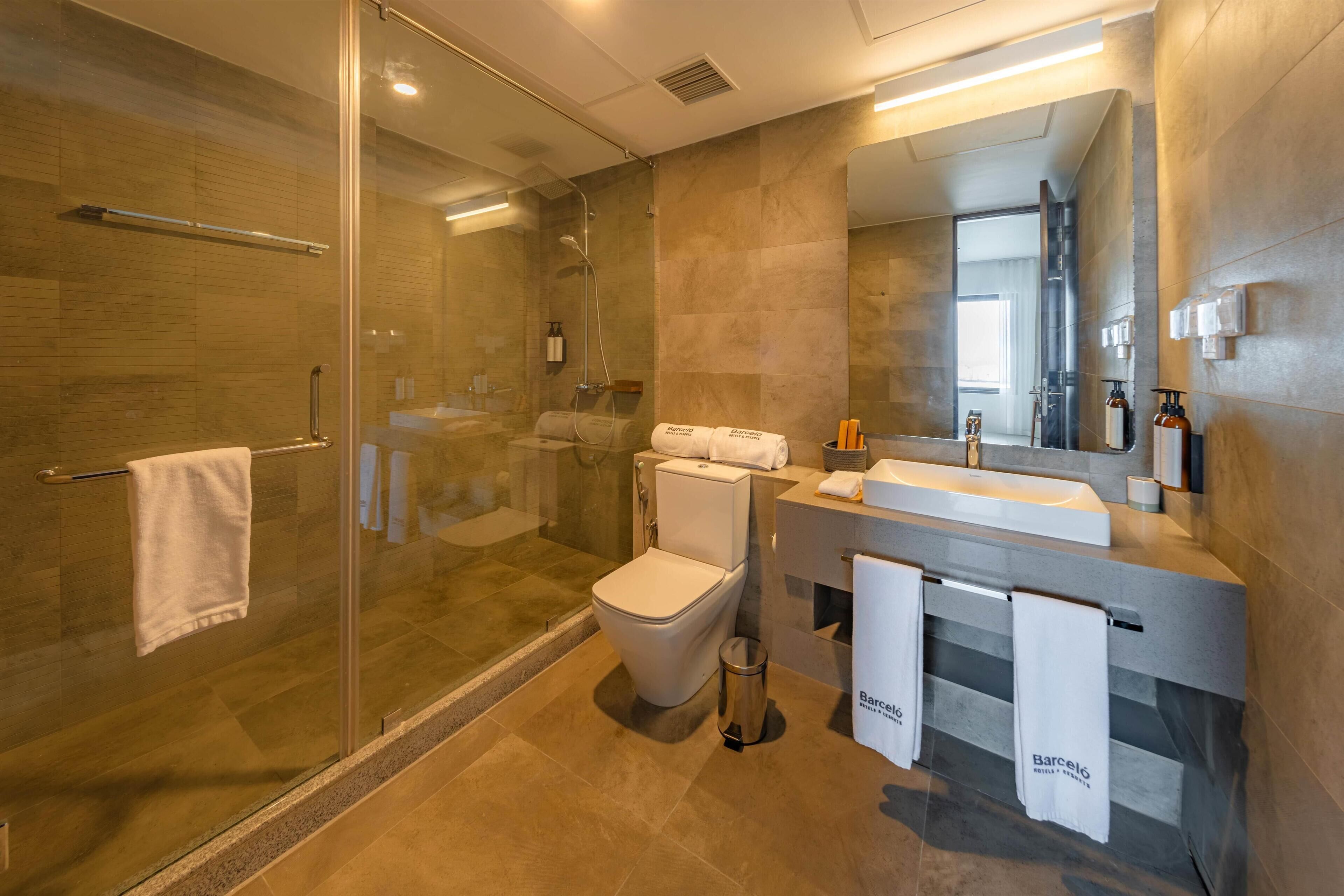 Un baño moderno con ducha envuelta en vidrio, inodoro, lavabo y un espejo grande.