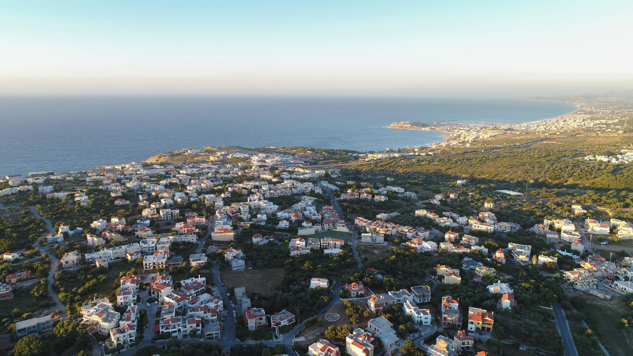Vista aérea de uma área residencial costeira com casas, ruas e uma orla marítima.