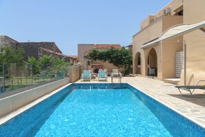 A swimming pool with lounge chairs and a covered seating area, surrounded by buildings with a Mediterranean architectural style. - Abrakamus By Forest Villas (Rethymno)