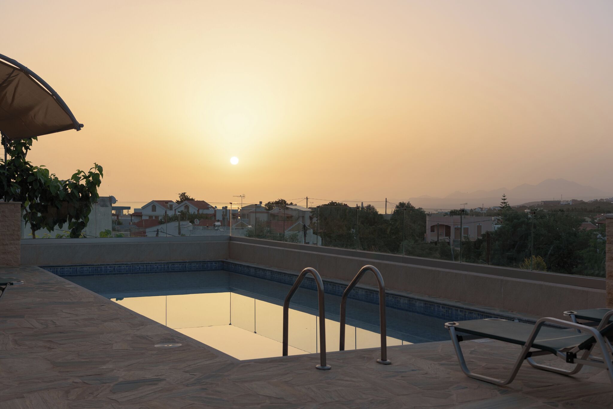 A rooftop swimming pool with a view of the sunset and surrounding buildings.