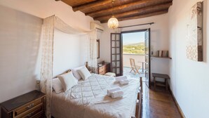 A bedroom with a wooden ceiling, a bed with white linens, a bedside table, a chair, and a view of the outdoors. - Abrakamus By Forest Villas (Rethymno)