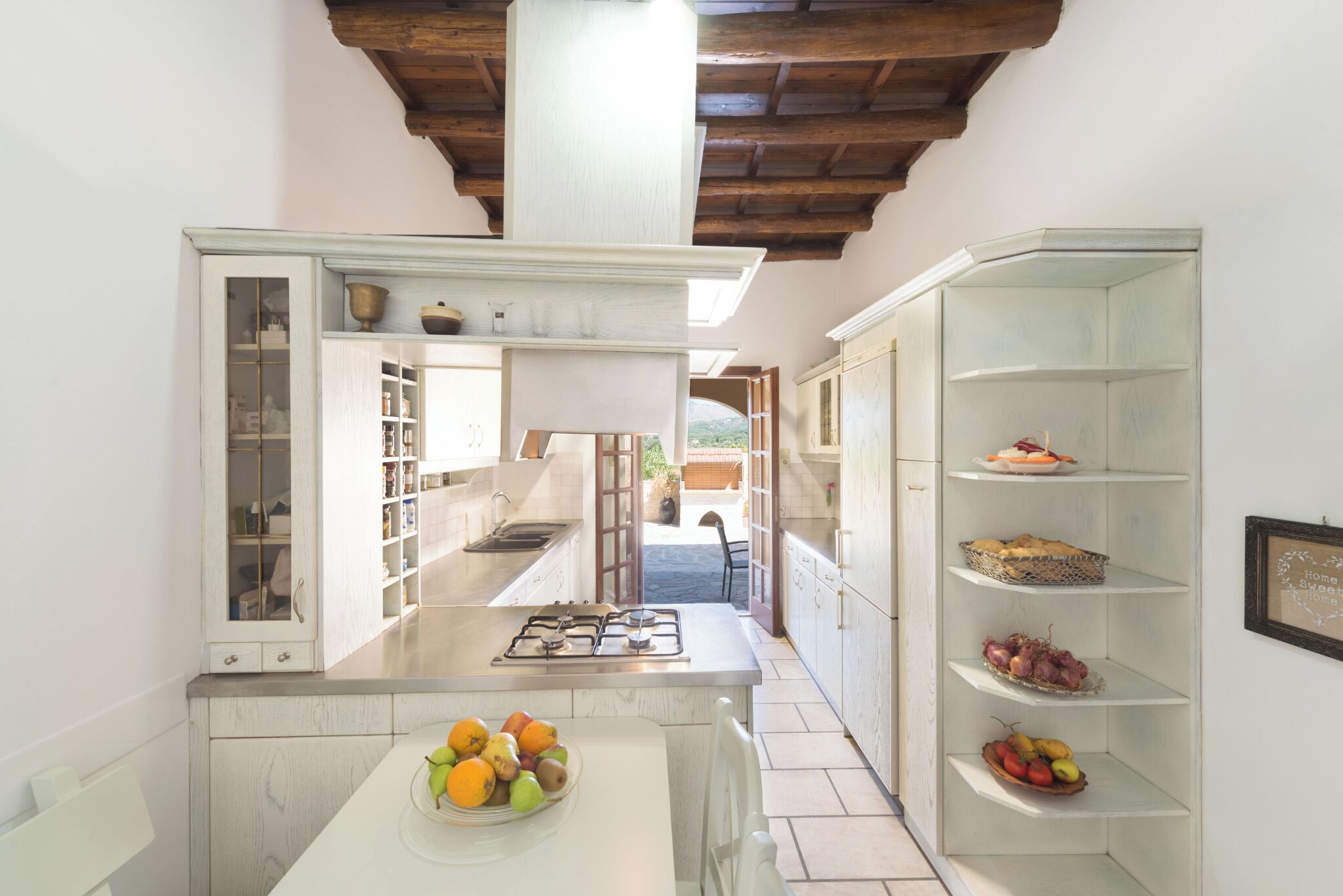 Cocina con muebles blancos, una isla central con estufa a gas y vistas a un espacio exterior.