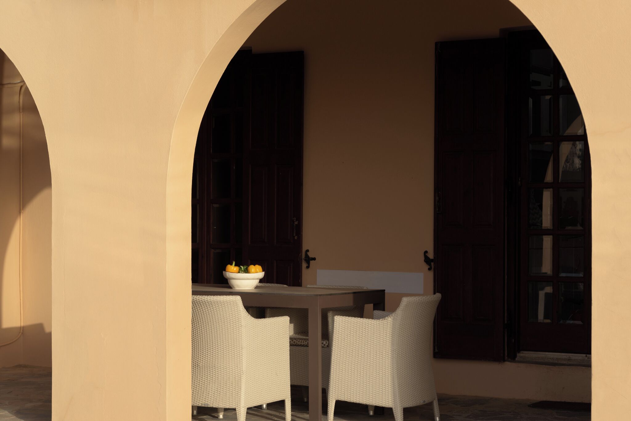 Een terras buiten met een tafel, twee stoelen, een schaal fruit en een deur met een openslaand luik.