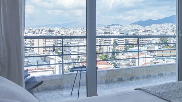 A hotel room with a large window offering a city view.