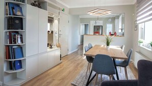 A modern dining area with a wooden table, grey chairs, and a bookshelf filled with books.