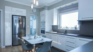 A modern kitchen with white cabinetry, a stainless steel refrigerator, a dining table with chairs, and a window with a view.