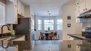 A modern kitchen with granite countertops, white cabinetry, and a dining area with a round table and chairs. - Midtown Urban Retreat- Family Friendly 3BR Retreat (Tallahassee)