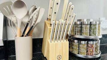 Una encimera de cocina con un portalapilas que contiene cuchillos y cucharas, una taza blanca y frascos de especias.