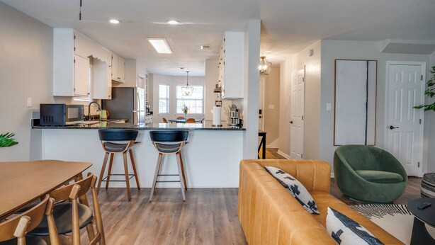 A modern kitchen with a central island, bar stools, and a dining area with a wooden table and chairs. - Midtown Urban Retreat- Family Friendly 3BR Retreat (Tallahassee)
