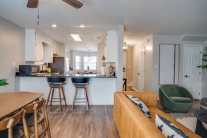 Una cocina moderna con una isla central, taburetes de bar y un comedor con mesa y sillas de madera.