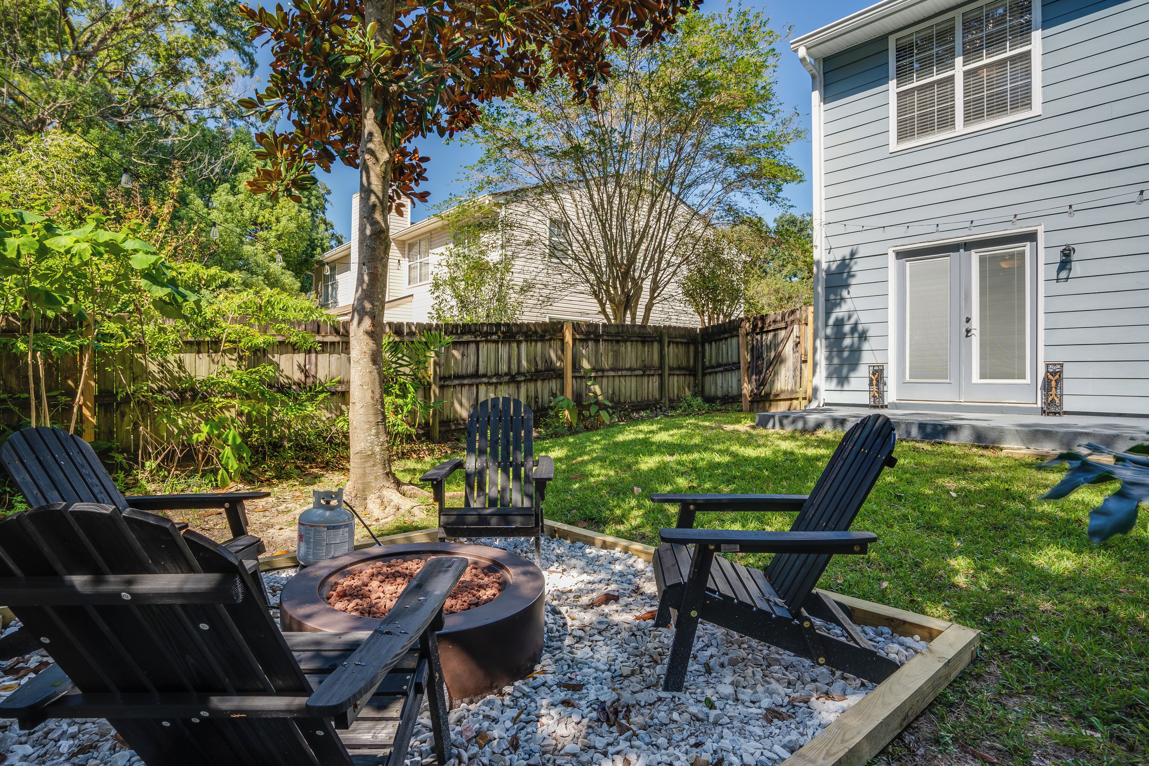 A backyard with a fire pit, three Adirondack chairs, and a wooden deck.